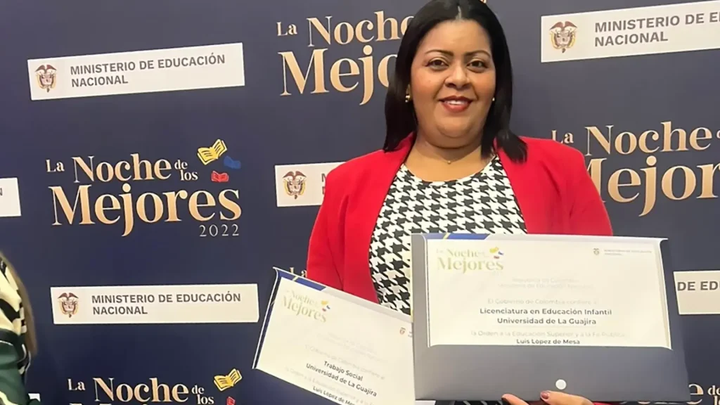 Una mujer sonriente, vestida con una chaqueta roja y una blusa de cuadros, sosteniendo dos certificados en un evento llamado "La Noche de los Mejores".