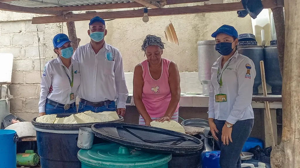 Cuatro personas adultas posan con tanques de queso en un entorno rural.