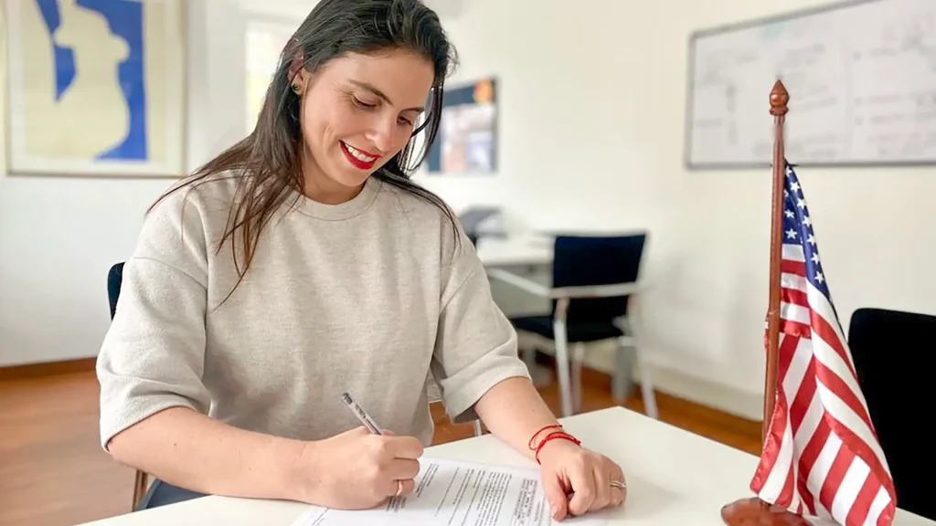 Mujer adulta sentada en un escritorio firmando un papel. 