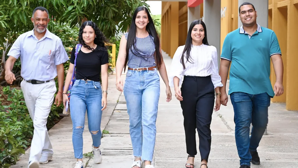Grupo de cinco personas de diferentes edades caminando en el campus universitario.
