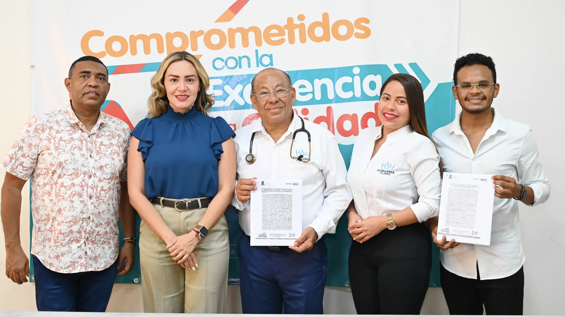 Cinco personas de pie posando para una foto, dos de ellos sostienen un papel en sus manos.