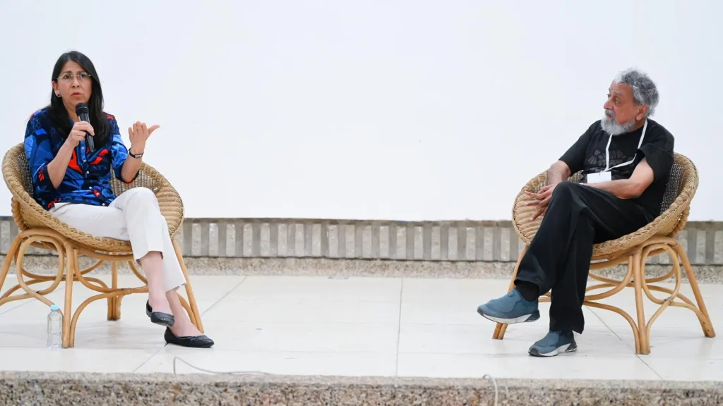 Un hombre y una mujer sentados en la tarima de un auditorio, hablan frente al público.