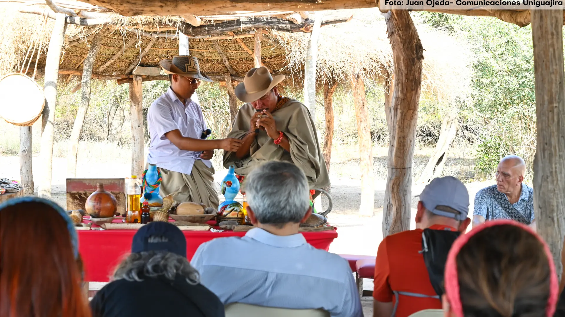 Dos hombres indígenas dialogando uno interpreta un instrumento