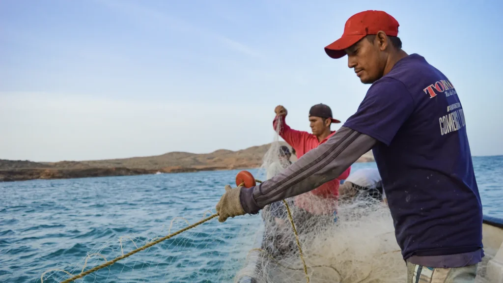 Dos hombres indígenas tirando una red de pesca al mar