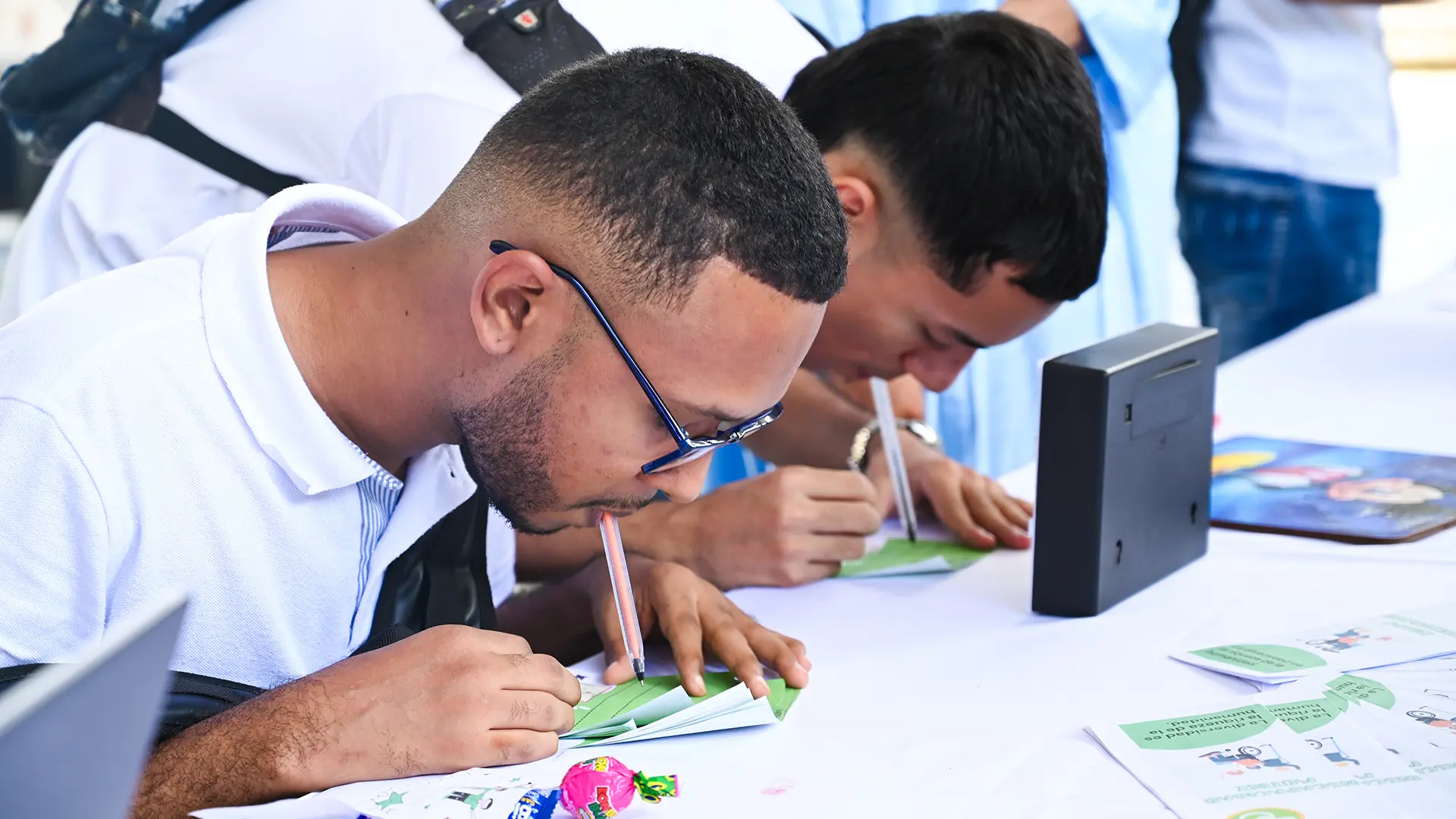 Dos estudiantes escribiendo en un papel, sujetando el lápiz con la boca.