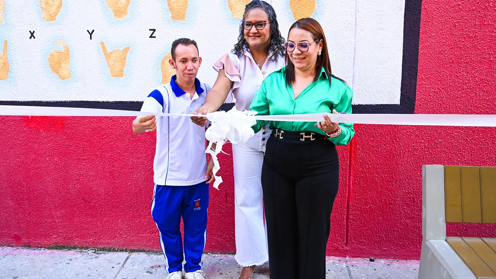 Dos mujeres y un hombre cortando la cinta del mural.