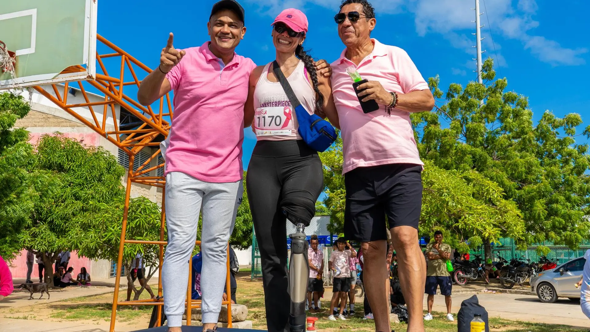 Tres personas, dos hombres y una mujer con una prótesis en la pierna, sonríen en el escenario tras finalizar la carrera rosa, todos vestidos de rosa.