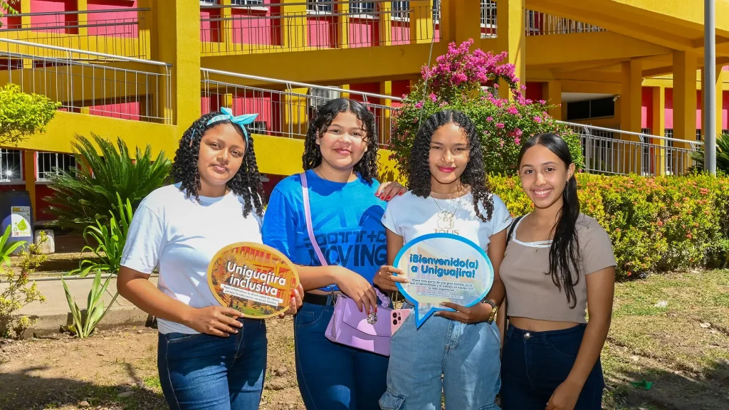 Grupo de cinco estudiantes nuevos en la sede Fonseca de la Universidad de La Guajira, posando al aire libre con carteles motivacionales.
