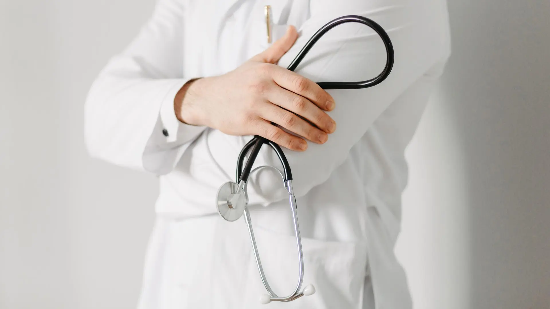 Médico con bata blanca sosteniendo un estetoscopio en sus brazos.