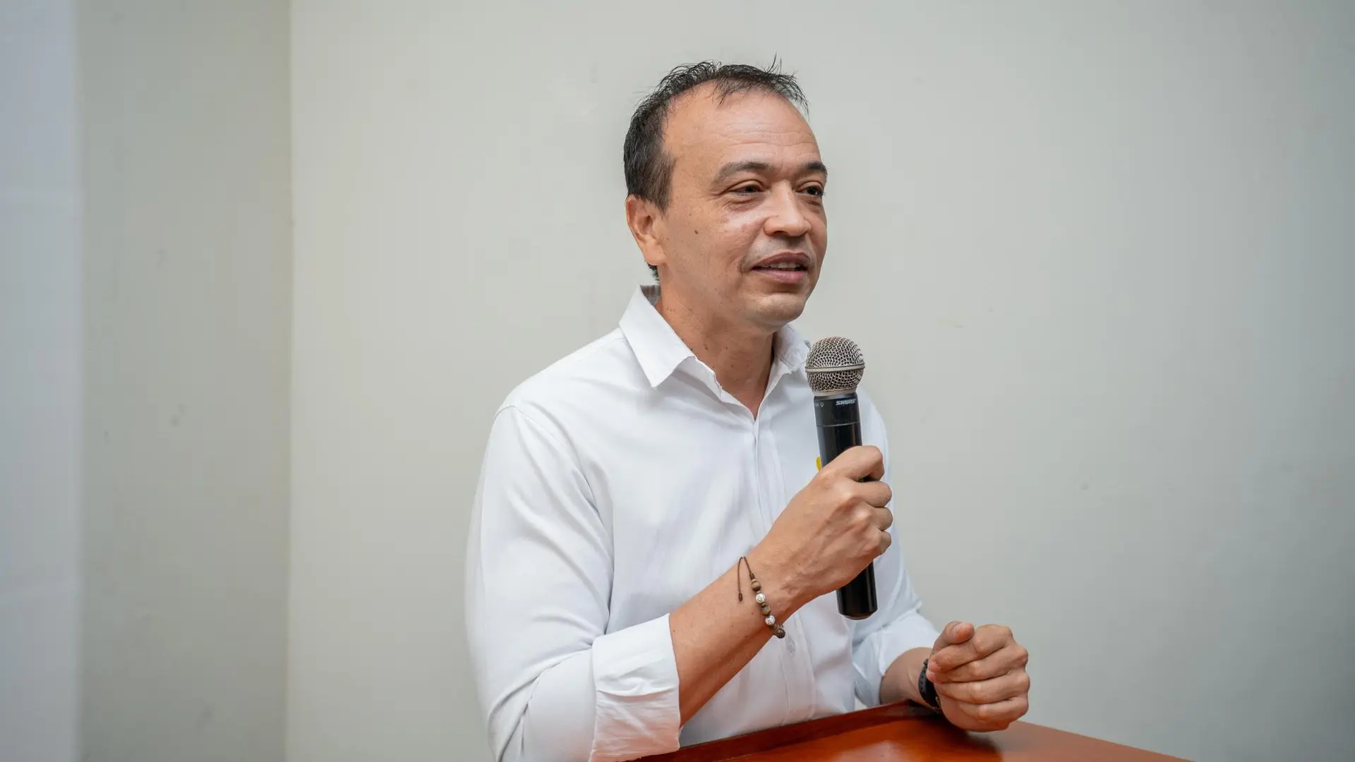 Hombre de camisa blanca habla al público con micrófono en mano durante un evento.