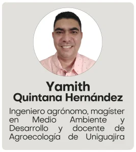 Yamith Quintana Hernandez Hombre de cabello corto y oscuro, piel trigueña, sonriente, viste una camisa rosada con pequeños puntos en colores azul y rojo. Está de pie frente a una pared blanca, mirando a la cámara.