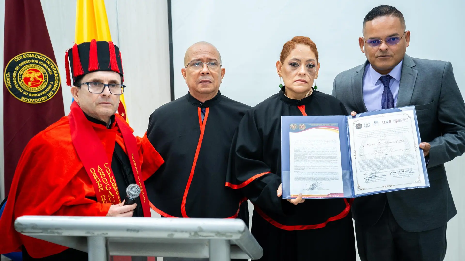 Grupo de personas vestidas con togas y birretes negros con detalles rojos posan para una fotografía grupal durante una ceremonia académica. En primera fila hay personas sonriendo, algunas con bandas rojas o amarillas que indican “Doctor HC”.