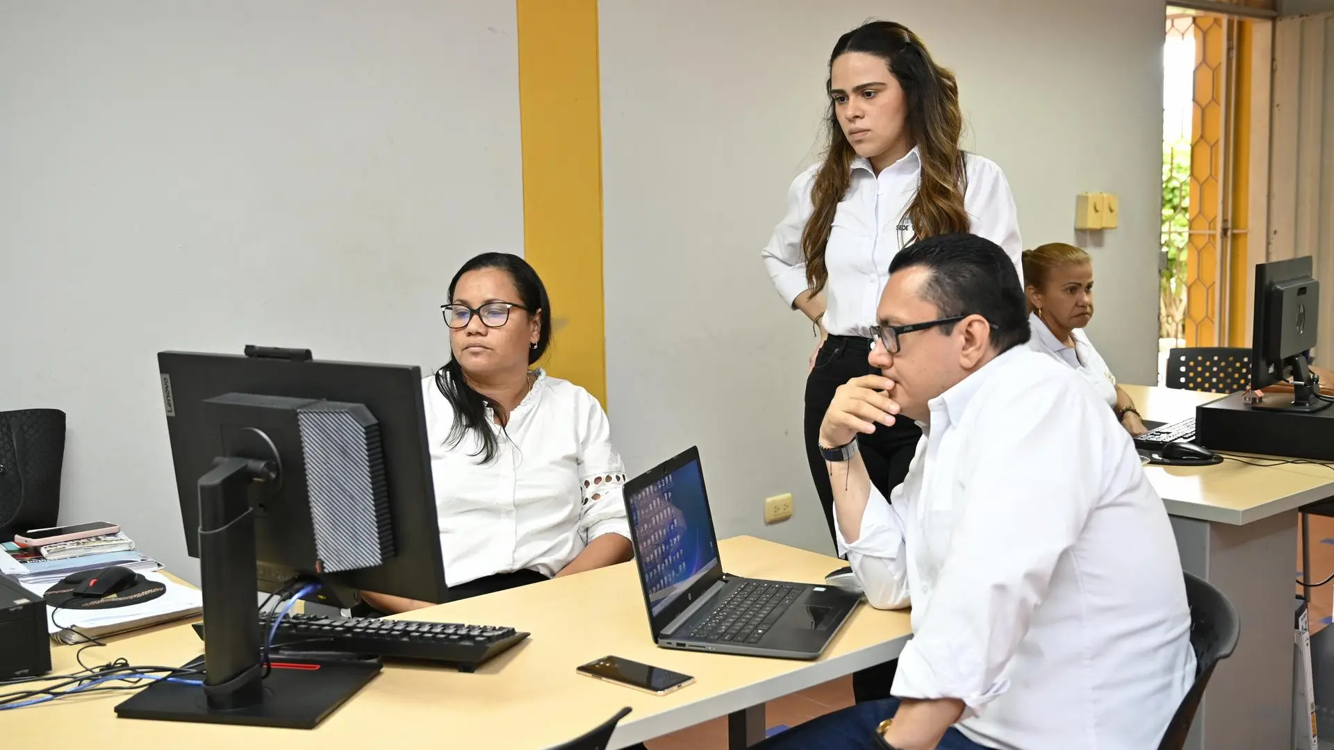 Equipo de trabajo de la Universidad de La Guajira frente a computadores en una sala. Cuatro personas, vestidas de blanco, revisan información en pantalla como parte de la auditoría externa.