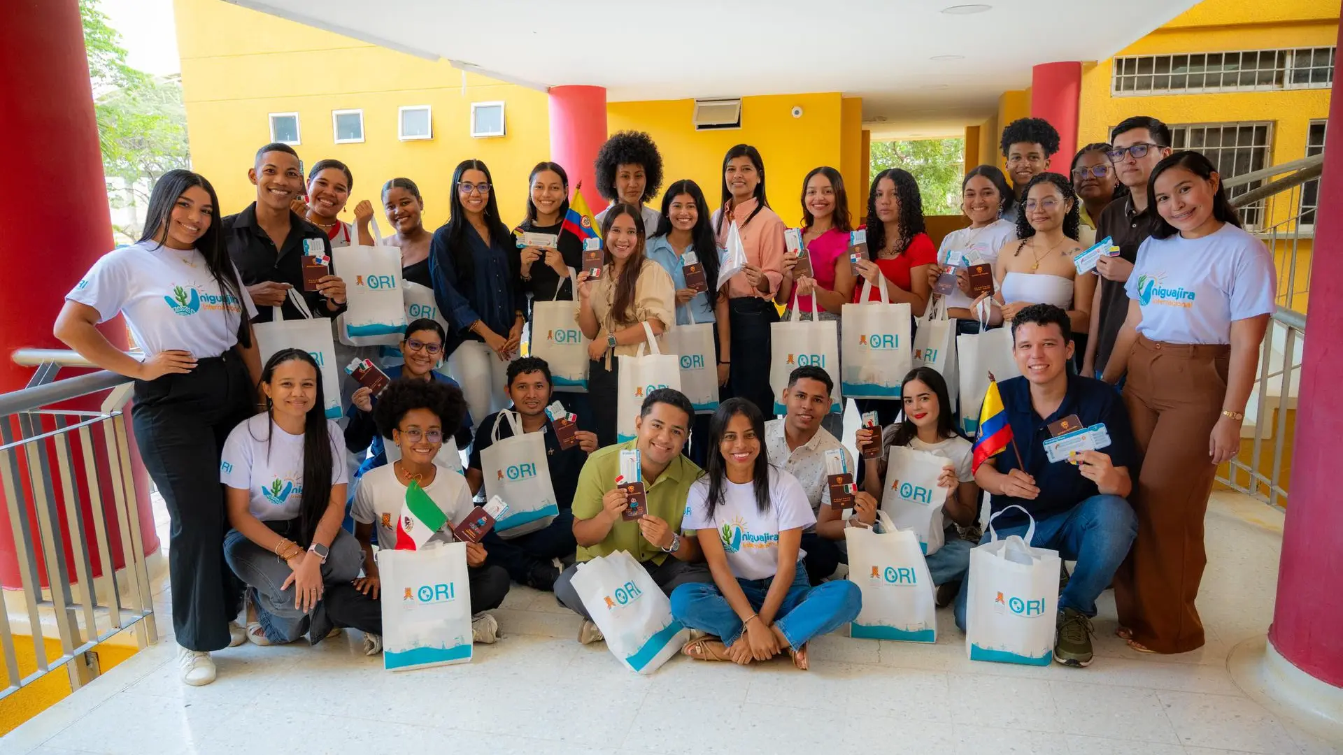 Grupo de estudiantes universitarios reunidos en un espacio académico durante una actividad de internacionalización. Los participantes sostienen pasaportes, banderas y kits institucionales, reflejando oportunidades de movilidad académica, intercambio cultural y proyección internacional.