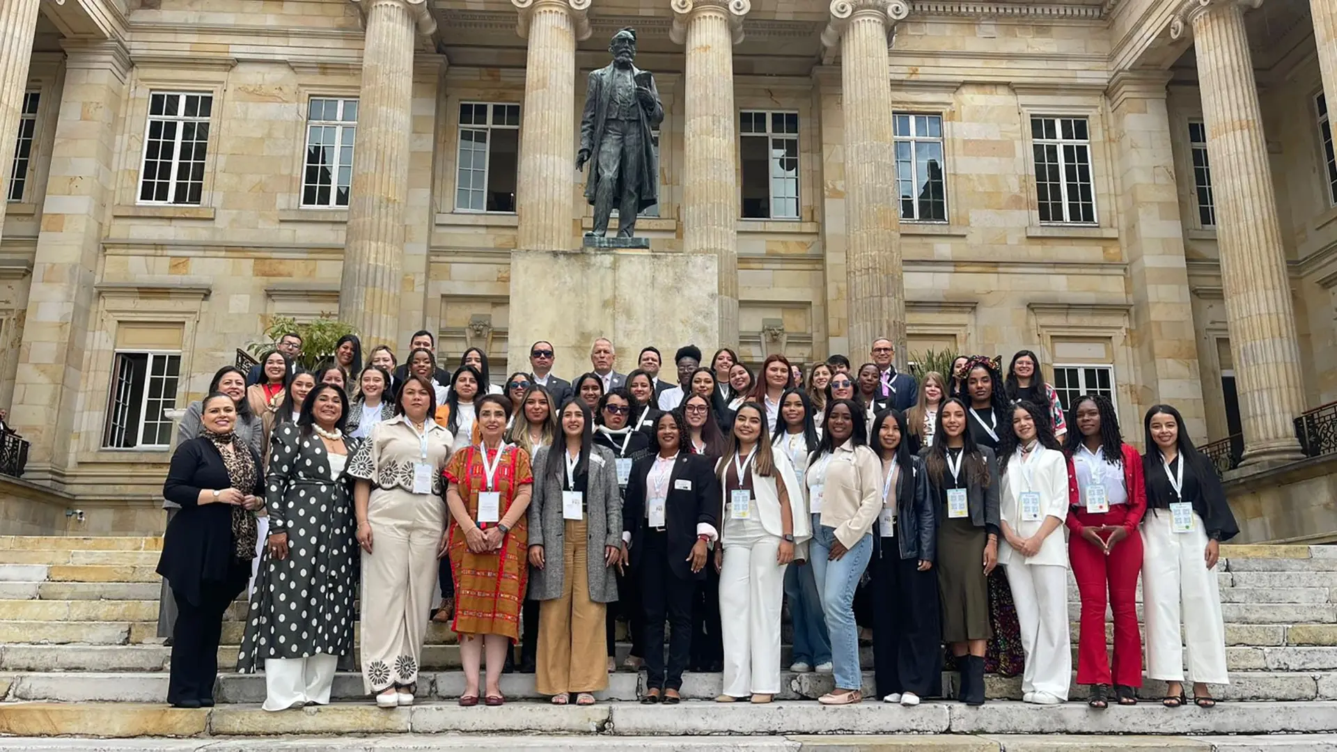 Gran grupo de participantes posando en las escaleras de un edificio institucional con columnas y una estatua al fondo.