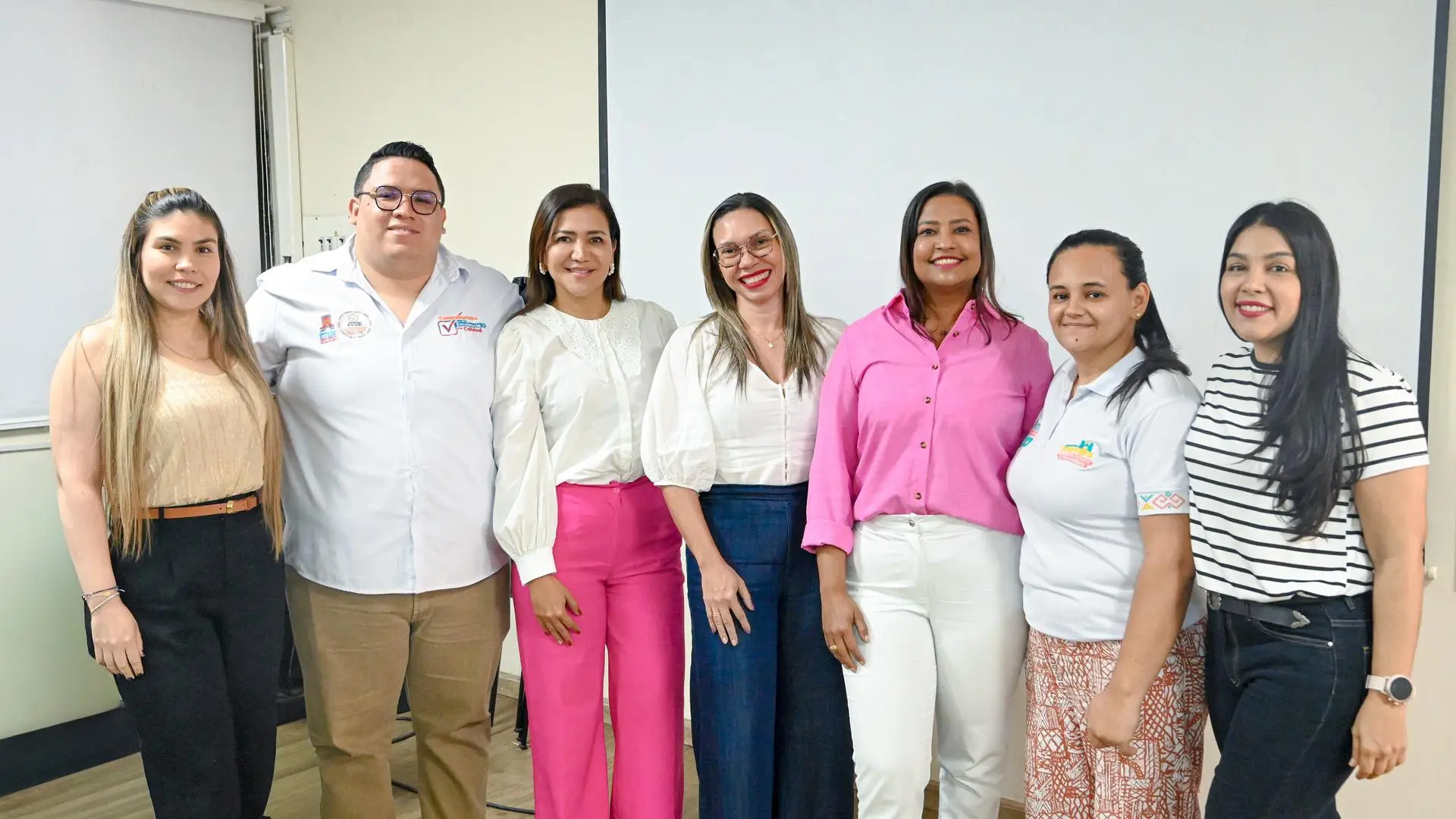 Grupo de siete personas adultas, hombres y mujeres, posando de pie en un aula de clases con proyector al fondo. Todos miran a la cámara y sonríen.