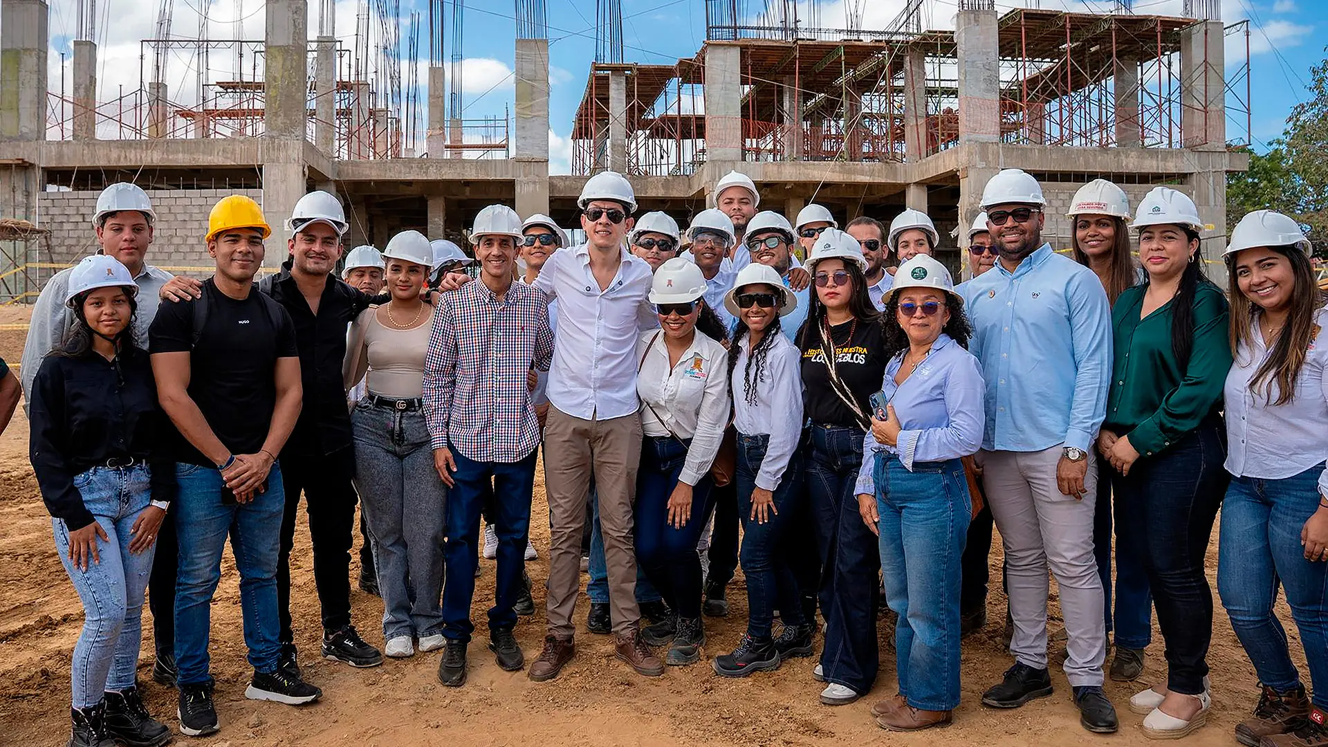 Un grupo de hombres y mujeres posan con cascos en un espacio abierto.Al fondo se observa una estructura o edificación en construcción