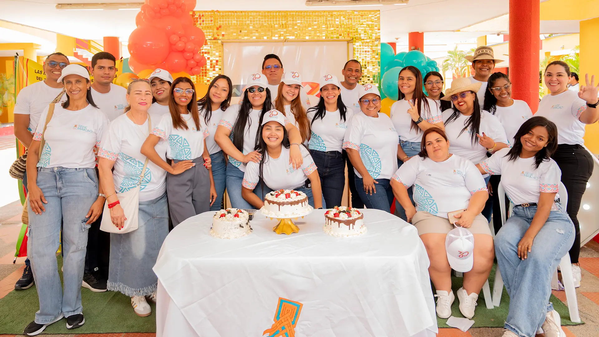 Grupo de funcionarios y colaboradores de la Universidad de La Guajira, Sede Maicao, reunidos alrededor de una mesa con tortas en un espacio decorado, durante la conmemoración de aniversario institucional.