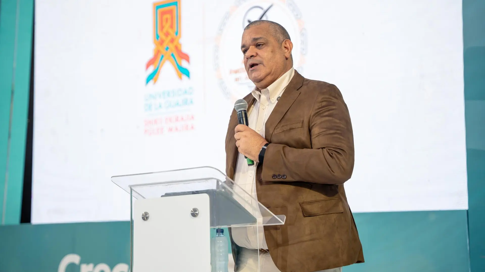 Hombre ofrece una conferencia desde un podio durante un evento institucional de la Universidad de La Guajira.