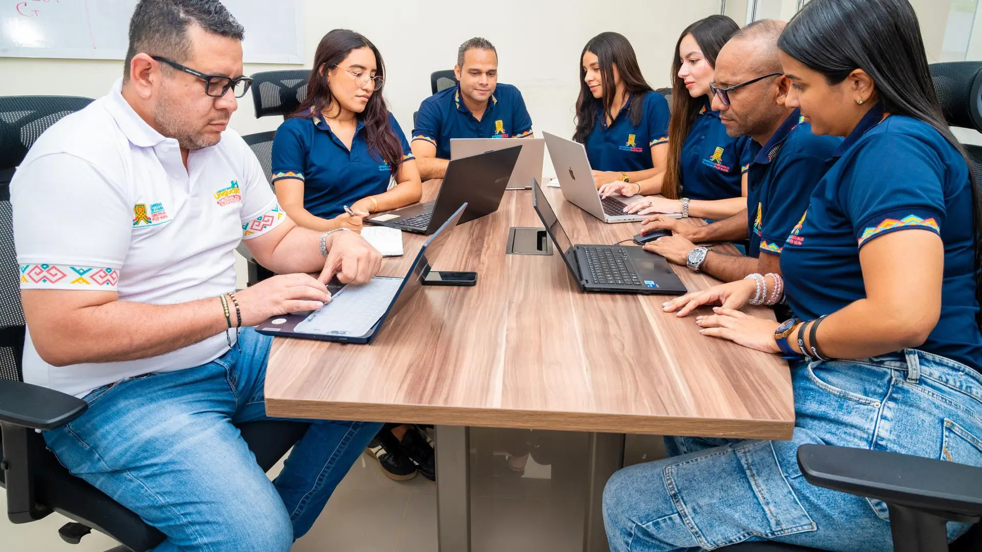 Equipo de colaboradores universitarios reunidos en una sala de juntas trabajando de manera colaborativa con computadores portátiles. La escena refleja planificación institucional, trabajo en equipo y desarrollo de proyectos académicos y administrativos en un entorno profesional.