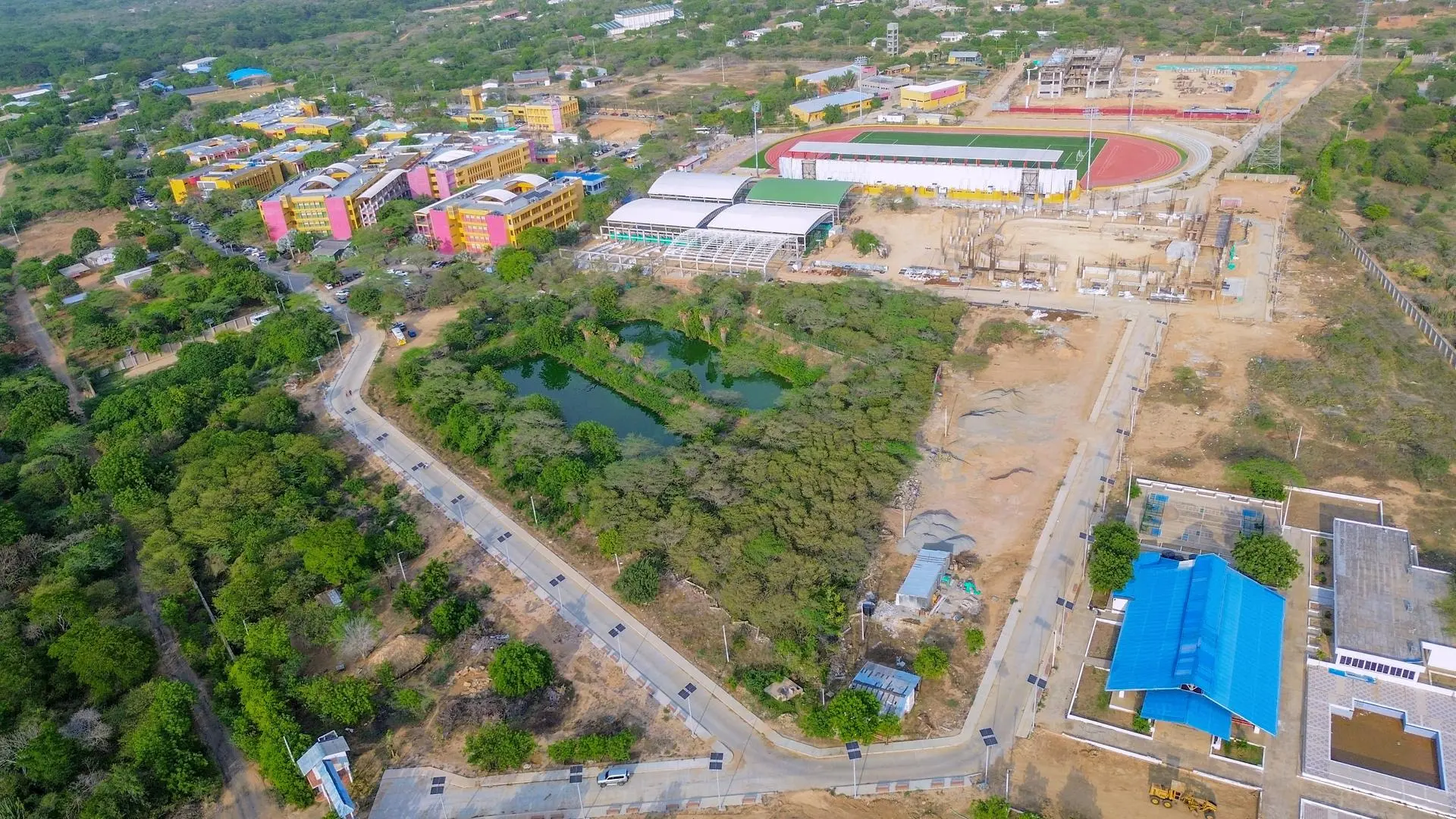 Fotografía aérea de un campus universitario rodeado de zonas verdes, donde se observan edificios académicos, instalaciones deportivas y proyectos de infraestructura en desarrollo. La imagen resalta el crecimiento institucional y la integración entre educación, urbanismo y entorno natural.