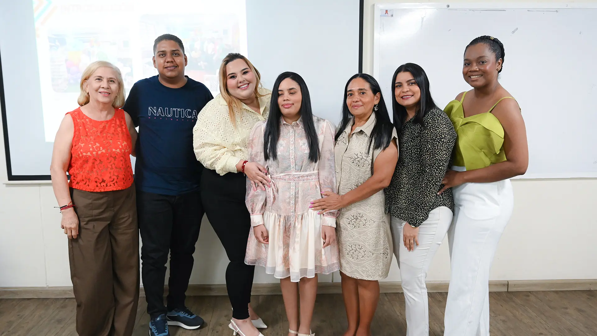 Grupo de siete personas posa para una fotografía al finalizar una presentación académica, frente a una pantalla de proyección y un tablero en un aula de la Universidad de La Guajira, Sede Maicao.