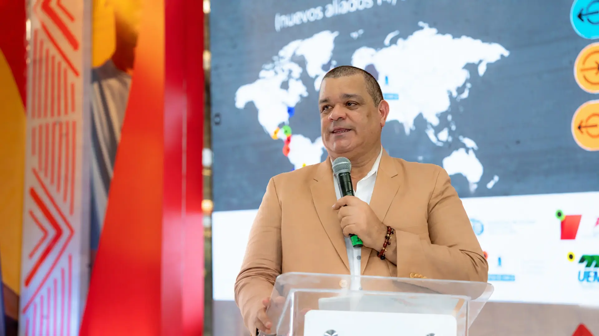 Rector Carlos Arturo Robles Julio durante una intervención en un evento académico, dirigiéndose al público con un micrófono frente a una pantalla con un mapa mundial y elementos gráficos relacionados con la internacionalización.