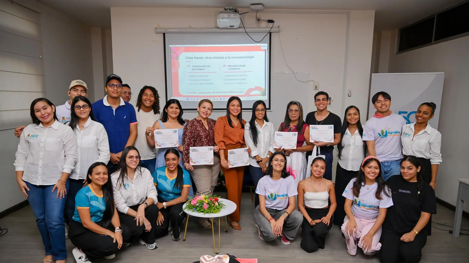 Estudiantes y docentes participan en una jornada académica sobre neuropsicología, posando con certificados de participación frente a una presentación sobre fundamentos psicológicos y neuropsicología.